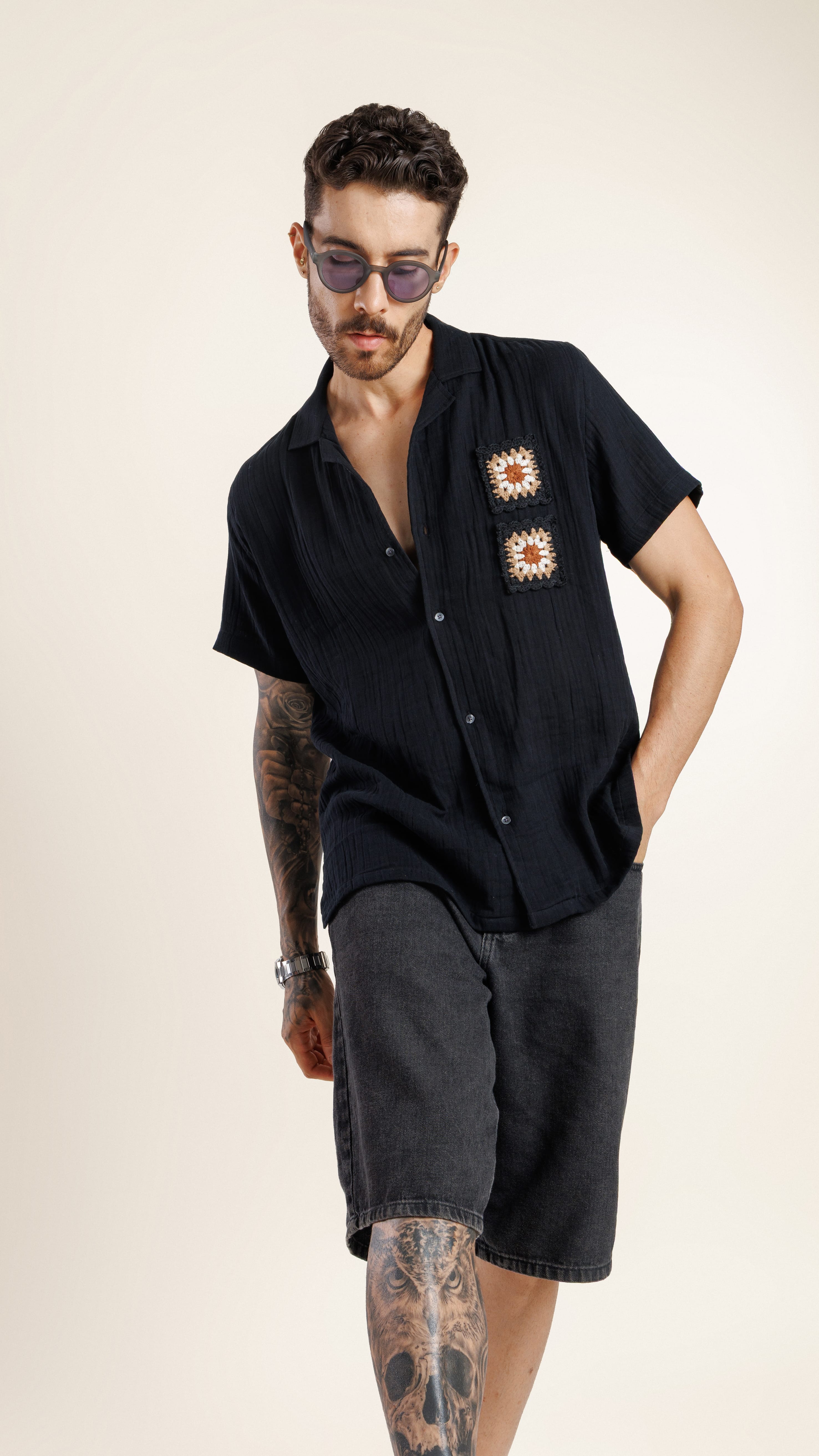 Man wearing a black shirt with floral designs and dark shorts on a beige background